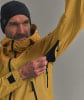 Ein Mann in einer gelben Jacke und schwarzer Mütze öffnet einen Reißverschluss am Ärmel.