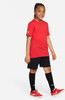 Junge in rotem T-Shirt, schwarzer Hose und Socken mit Turnschuhen.