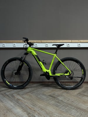 Ein grünes E-Bike mit schwarzen Rädern steht auf einem Holzboden vor einer grauen Wand. Ein grünes E-Bike mit schwarzen Rädern steht auf einem Holzboden vor einer grauen Wand.