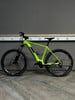 Ein grünes E-Bike mit schwarzen Rädern steht auf einem Holzboden vor einer grauen Wand.
