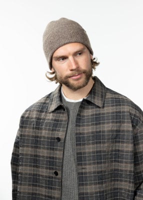Junger Mann mit brauner Mütze und kariertem Hemd über grauem Pullover.