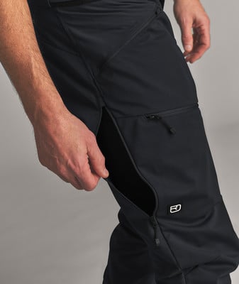 Eine männliche Hand greift in die offene Seitentasche einer schwarzen Hose.
