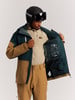 Ein Mann in einer Skijacke und einem Helm untersucht die Innentaschen der Jacke.