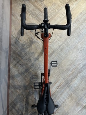 Ein orangefarbenes Fahrrad mit schwarzem Lenker und Sattel auf Holzuntergrund. Ein orangefarbenes Fahrrad mit schwarzem Lenker und Sattel auf Holzuntergrund.