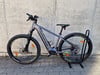 Graues Genesis E-Mountainbike auf einem Ständer vor einer Wand.