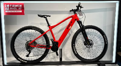 Rotes BH Mountain-E-Bike mit Schriftzug am Rahmen und Logo auf Fahne. Rotes BH Mountain-E-Bike mit Schriftzug am Rahmen und Logo auf Fahne.