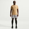 Ein Mann in einem beigefarbenen T-Shirt und grauen Shorts steht vor einem weißen Hintergrund.