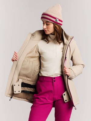 Eine Frau in einer beigen Jacke und pinker Hose mit Mütze.