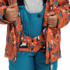 Kind in oranger Winterjacke mit Pinguinen und blauer Latzhose.