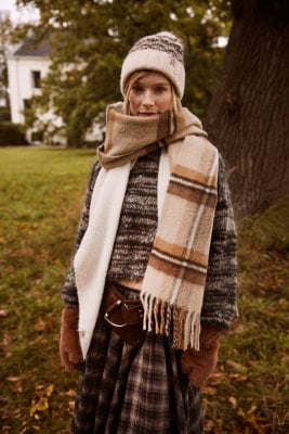 Eine Frau in einer Beanie und kariertem Schal posiert im Freien. Eine Frau in einer Beanie und kariertem Schal posiert im Freien.