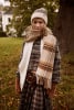 Eine Frau in einer Beanie und kariertem Schal posiert im Freien.