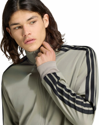 Ein Mann in einer grauen Jacke mit schwarzen Streifen an den Ärmeln.