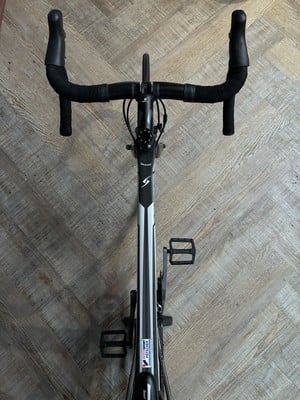 Ein Rennrad mit schwarzem Lenker und weiß-schwarzem Rahmen auf Holzboden. Ein Rennrad mit schwarzem Lenker und weiß-schwarzem Rahmen auf Holzboden.