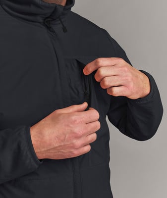 Ein Mann verstellt den Reißverschluss einer dunklen Jacke, seine Hände sind nahe der Tasche. Ein Mann verstellt den Reißverschluss einer dunklen Jacke, seine Hände sind nahe der Tasche.