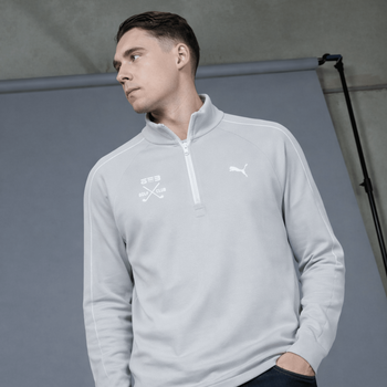 Mann in grauem Puma-Pullover mit Golfschlägern