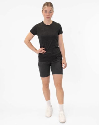 Eine Frau in einem dunklen T-Shirt und Shorts steht vor einem weißen Hintergrund. Eine Frau in einem dunklen T-Shirt und Shorts steht vor einem weißen Hintergrund.