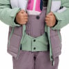 Ein Mädchen schließt seine Winterjacke über einer Latzhose.