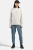 Ein Mann mit schwarzer Kappe trägt einen beigen Pullover und blaue Hose.