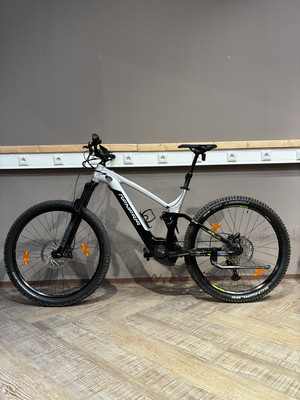 Ein Genesis E-Mountainbike mit Federung und schwarzen Rädern auf Holzboden. Ein Genesis E-Mountainbike mit Federung und schwarzen Rädern auf Holzboden.