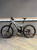 Ein Genesis E-Mountainbike mit Federung und schwarzen Rädern auf Holzboden.