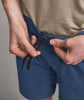 Männliche Hände ziehen die Kordel einer blauen Hose fest.