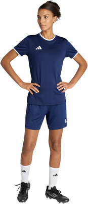 Eine Frau in einem dunkelblauen Fußballtrikot und Shorts mit weißen Socken und Fußballschuhen.