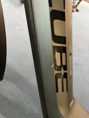 Detail eines E-Bike-Rahmens mit CUBE-Logo und kleiner Lackbeschädigung. Detail eines E-Bike-Rahmens mit CUBE-Logo und kleiner Lackbeschädigung.