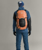 Ein Mann in Skibekleidung mit orangefarbenem Rucksack und schwarzem Helm.