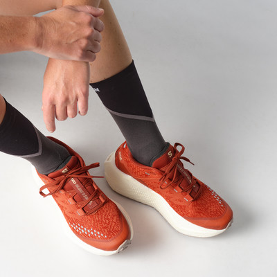 Zwei Beine in orangefarbenen Laufschuhen und dunklen Socken auf grauem Hintergrund. Zwei Beine in orangefarbenen Laufschuhen und dunklen Socken auf grauem Hintergrund.