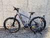 Ein graues Genesis E-Bike steht auf einem Ständer vor einer Betonwand.