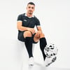 Ein Fußballspieler im schwarzen Trikot sitzt auf einem weißen Podest mit einem Ball.