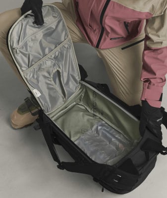 Ein offener schwarzer Rucksack mit Innentaschen und einer Person in Skibekleidung. Ein offener schwarzer Rucksack mit Innentaschen und einer Person in Skibekleidung.