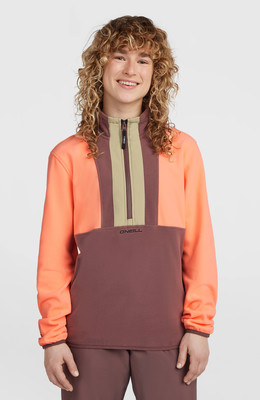 Mädchen mit lockigem Haar in einem orange-braunen Fleece-Pullover mit O'Neill-Logo. Mädchen mit lockigem Haar in einem orange-braunen Fleece-Pullover mit O'Neill-Logo.