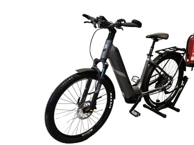 Ein graues E-Bike mit Schutzblechen und einem Ständer, an dem ein Feuerlöscher befestigt ist. Ein graues E-Bike mit Schutzblechen und einem Ständer, an dem ein Feuerlöscher befestigt ist.