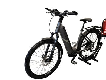 Ein graues E-Bike mit Schutzblechen und einem Ständer, an dem ein Feuerlöscher befestigt ist.