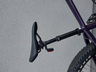 Schwarze Sattelstütze mit rotem Licht am Fahrrad vor einer grauen Wand.