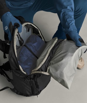 Eine Person packt eine blaue Jacke in einen schwarzen Rucksack. Eine Person packt eine blaue Jacke in einen schwarzen Rucksack.