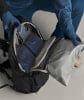 Eine Person packt eine blaue Jacke in einen schwarzen Rucksack.