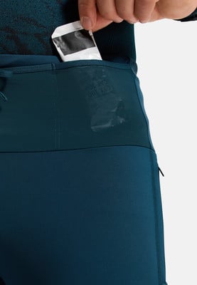 Eine Hand steckt einen kleinen Beutel in die Tasche einer Sporthose. Eine Hand steckt einen kleinen Beutel in die Tasche einer Sporthose.