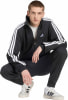 Ein Mann im schwarzen Adidas Trainingsanzug mit weißen Streifen an den Ärmeln.