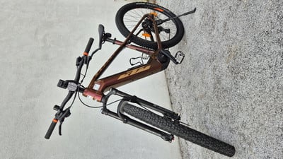 Ein braunes KTM E-Bike mit schwarzen Rädern und Gabel steht auf grauem Untergrund. Ein braunes KTM E-Bike mit schwarzen Rädern und Gabel steht auf grauem Untergrund.