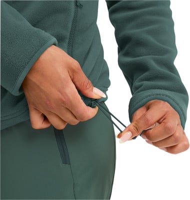 Eine Frau schließt den Reißverschluss einer dunkelgrünen Fleecejacke, um den Saum festzuziehen. Eine Frau schließt den Reißverschluss einer dunkelgrünen Fleecejacke, um den Saum festzuziehen.