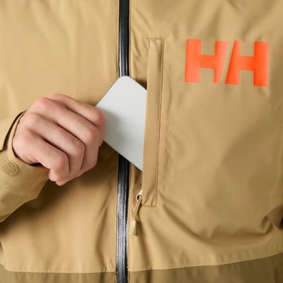 Egy kéz telefont tesz a HH logós kabát zsebébe. Egy kéz telefont tesz a HH logós kabát zsebébe.