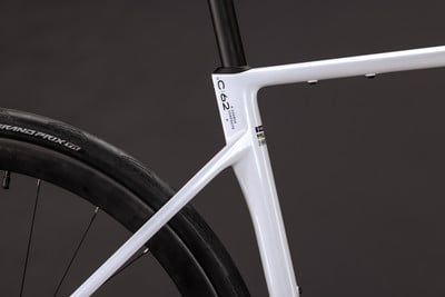 Detail eines weißen Carbon-Fahrradrahmens mit der Aufschrift C62 und einem Reifen. Detail eines weißen Carbon-Fahrradrahmens mit der Aufschrift C62 und einem Reifen.