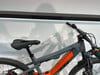 Graues E-Bike mit orangefarbenen Akzenten und schwarzem Sattel vor weißem Hintergrund.