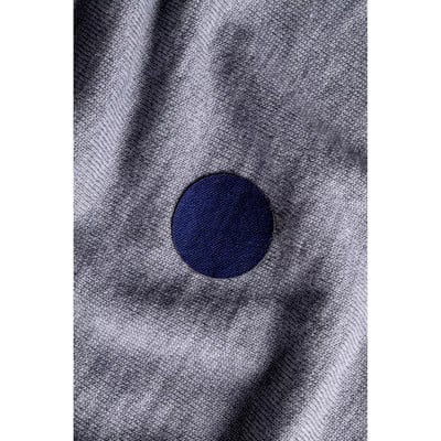 Ein dunkelblauer runder Aufnäher auf grauem Stoff mit feinem Muster. Ein dunkelblauer runder Aufnäher auf grauem Stoff mit feinem Muster.