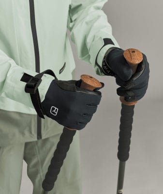 Eine Person hält Skistöcke in schwarzen Handschuhen und einer hellgrünen Jacke.