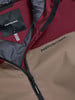 Detail einer Jacke mit Peak Performance Logo und Reißverschluss in Braun und Weinrot.