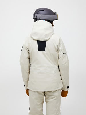 Rückansicht einer Person in einer beigen Skijacke und Hose mit Helm. Rückansicht einer Person in einer beigen Skijacke und Hose mit Helm.