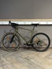 Ein grünes Gravelbike steht auf einem Holzboden vor einer grauen Wand.